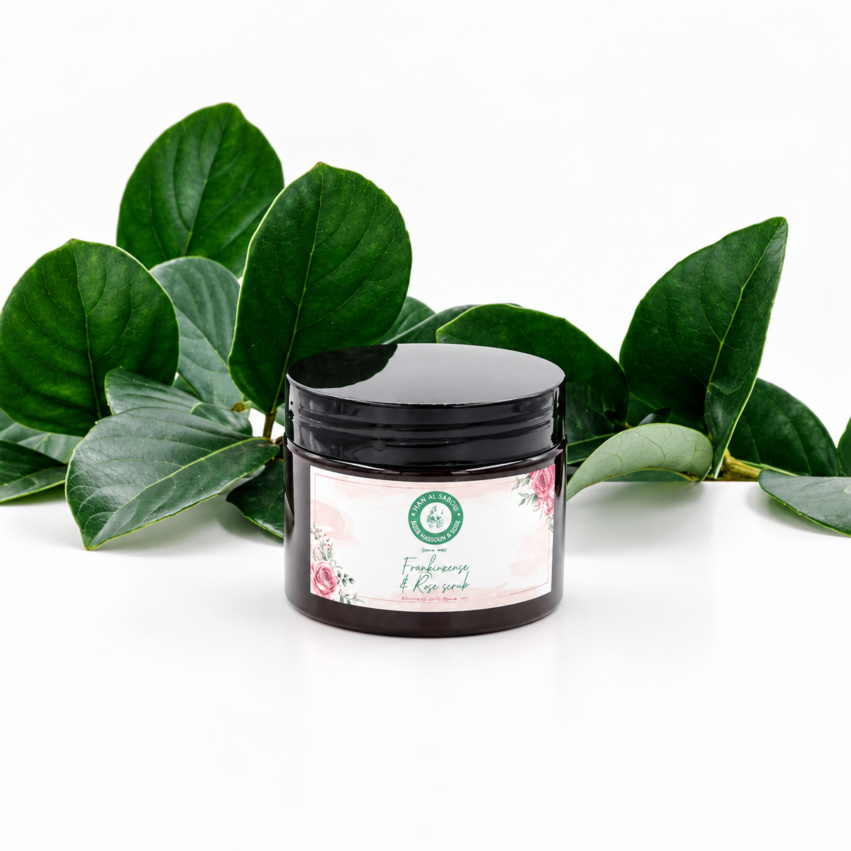 Khan Al Saboun Frankincense Face Scrub. Dark face scrub jar with a floral label and green foliage.