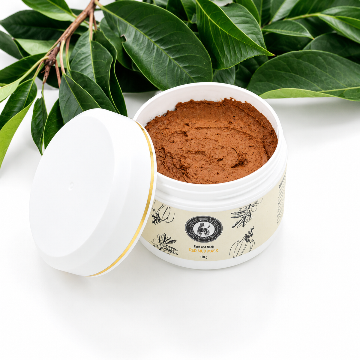 Khan Al Saboun Red Mud Mask – 150g. Open white jar of red mud mask with lid beside it and green leaves behind.