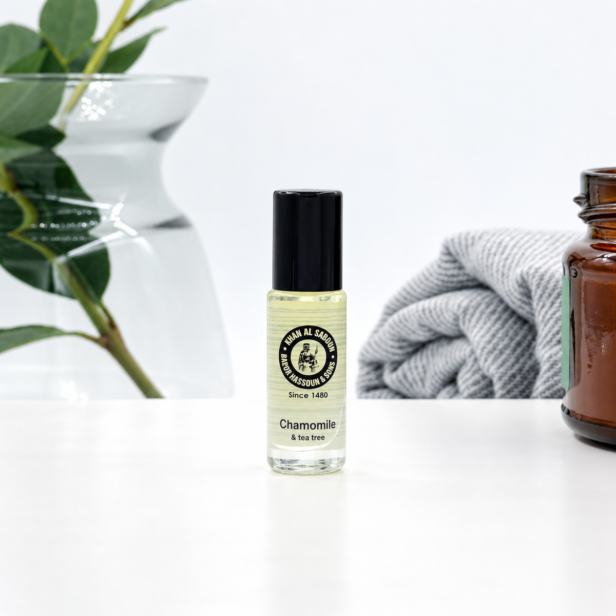 Khan Al Saboun Roll On Chamomile – 5ml. Chamomile roll-on bottle beside a glass vase, towel and amber jar.
