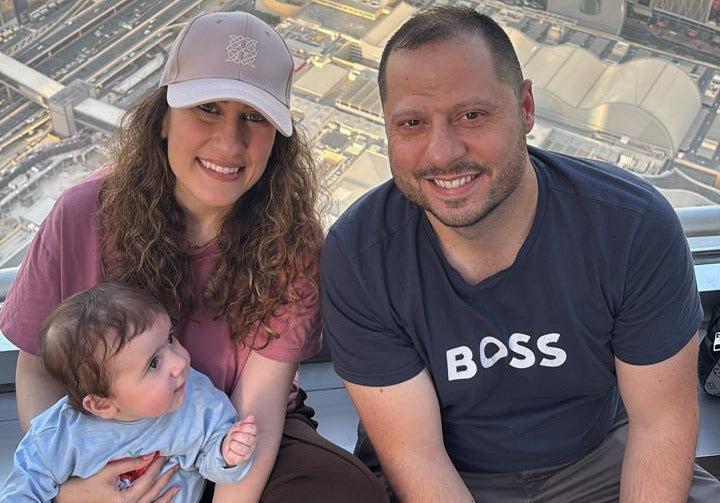 Family of three posing for a photo with a cityscape in the background