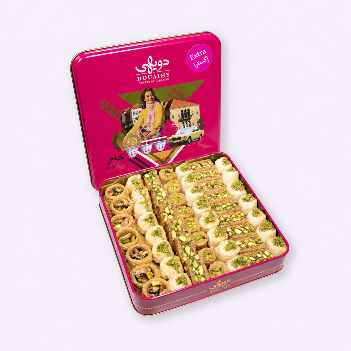 Douaihy assorted pistachio baklava in an open pink illustrated tin, with the original Douaihy branding, Extra badge and Arabic slogan حلو من لبنان.