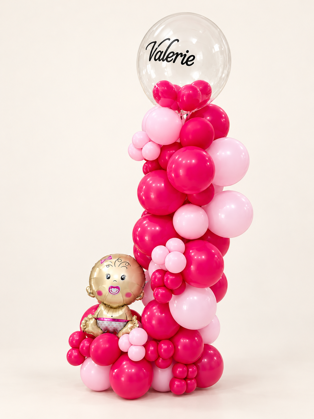 Personalized baby girl balloon tower with red and blush pink balloons, a clear name bubble and baby-girl foil balloon on an off-white background