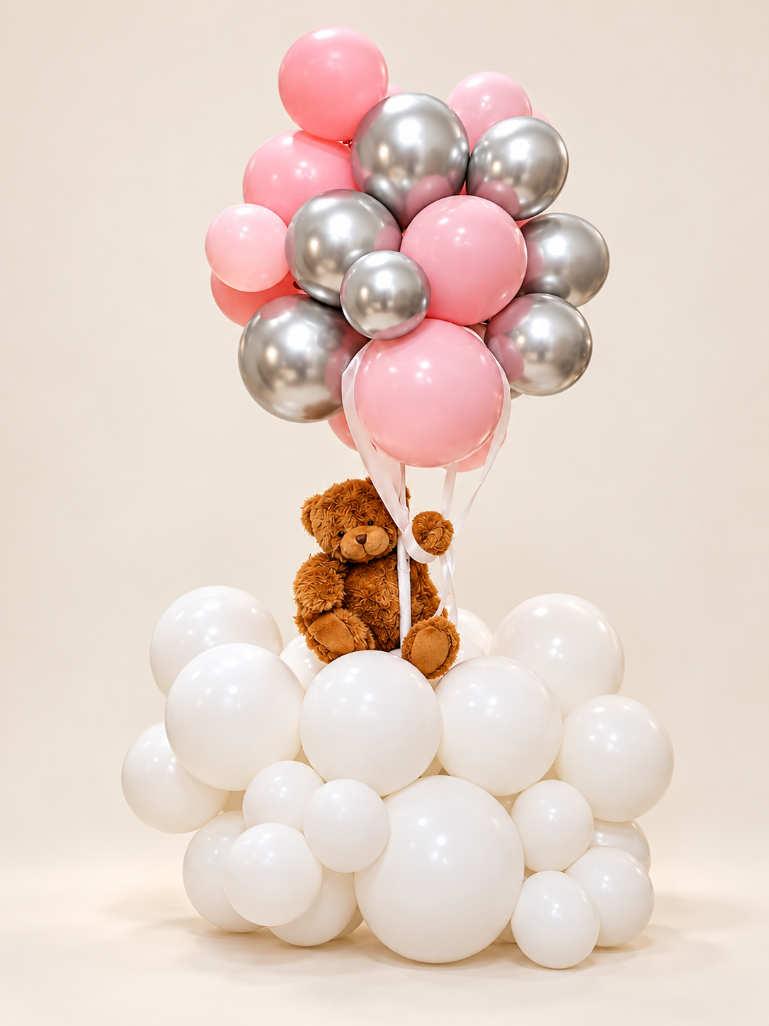 Silver Blush arrangement with pink and metallic silver balloons, white ribbons, a brown teddy bear and a white balloon base on an off-white background