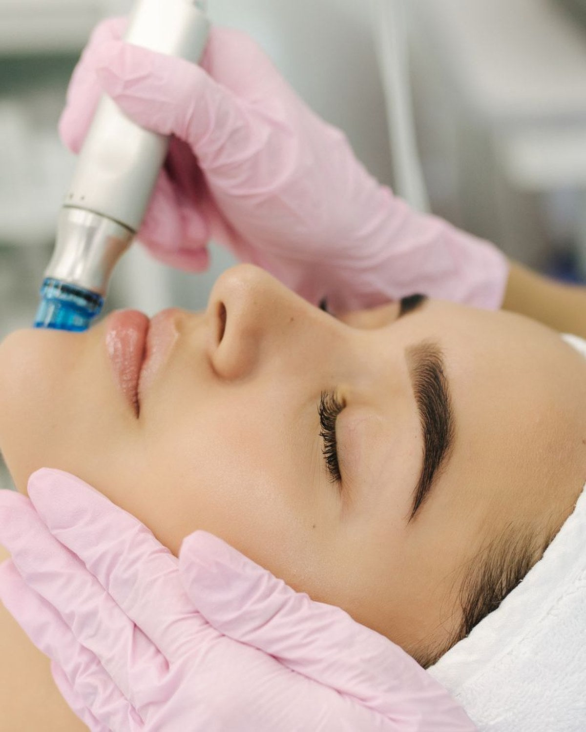Woman relaxing with eyes closed as a beautician glides a HydraFacial handpiece over her skin during a facial treatment