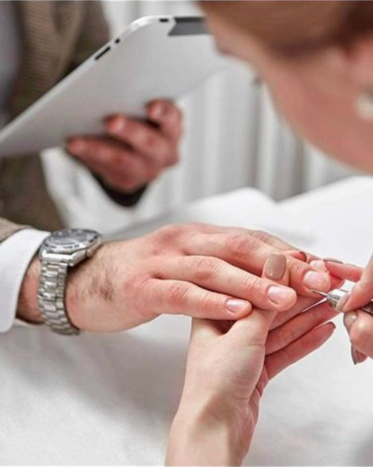Man in a tweed jacket relaxing while a nail technician gives him a professional manicure
