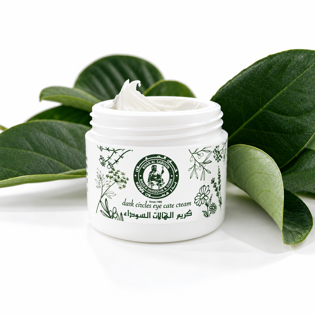 Khan Al Saboun Dark Circles Eye Cream. Open white eye cream jar with green botanical label and leaves behind.