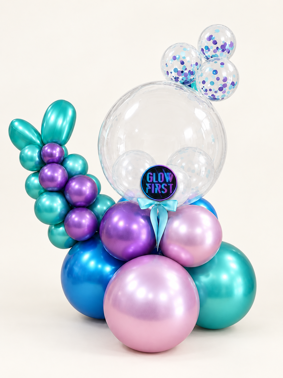 Aurora Glow balloon arrangement with a large clear bubble, confetti balloons, metallic teal, purple, lilac and blue balloons, and an aqua bow on an off-white background