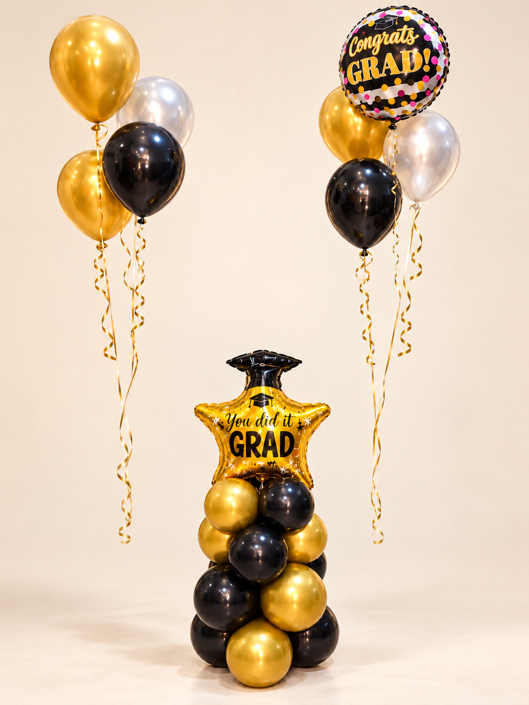 Golden Milestone black and gold graduation balloon column with star-shaped foil topper and floating gold, black and silver balloons with a Congrats GRAD foil balloon