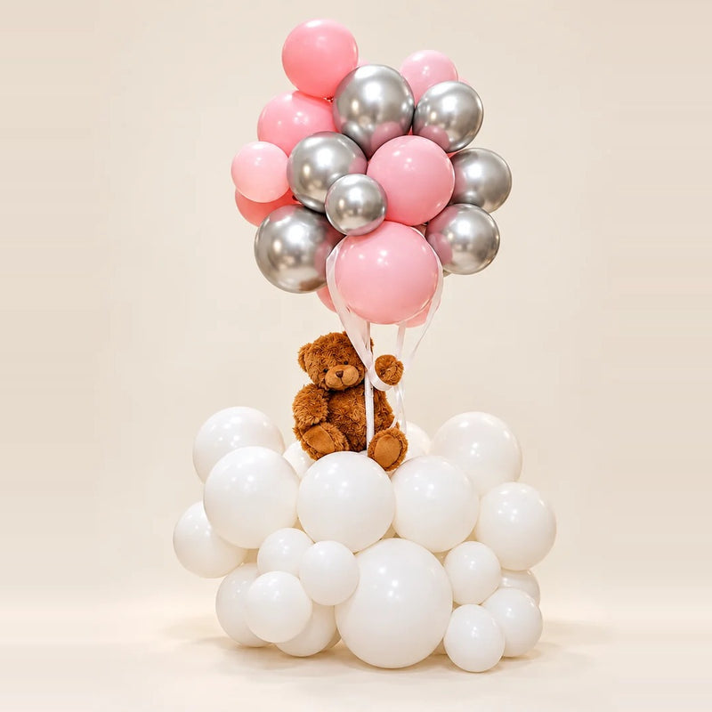 Pink and silver balloon bouquet floating above a teddy bear nestled in a cloud of white balloons