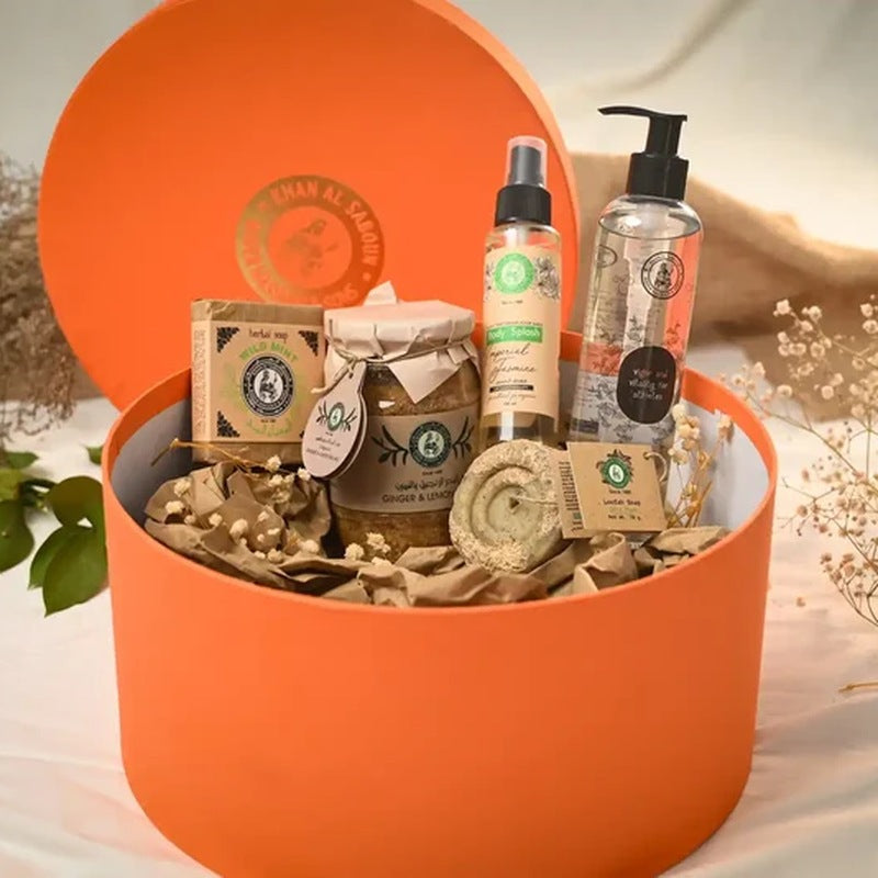 Open orange round gift box filled with Lebanese olive-oil soaps, a jar, natural sprays and a hand wash, surrounded by dried flowers