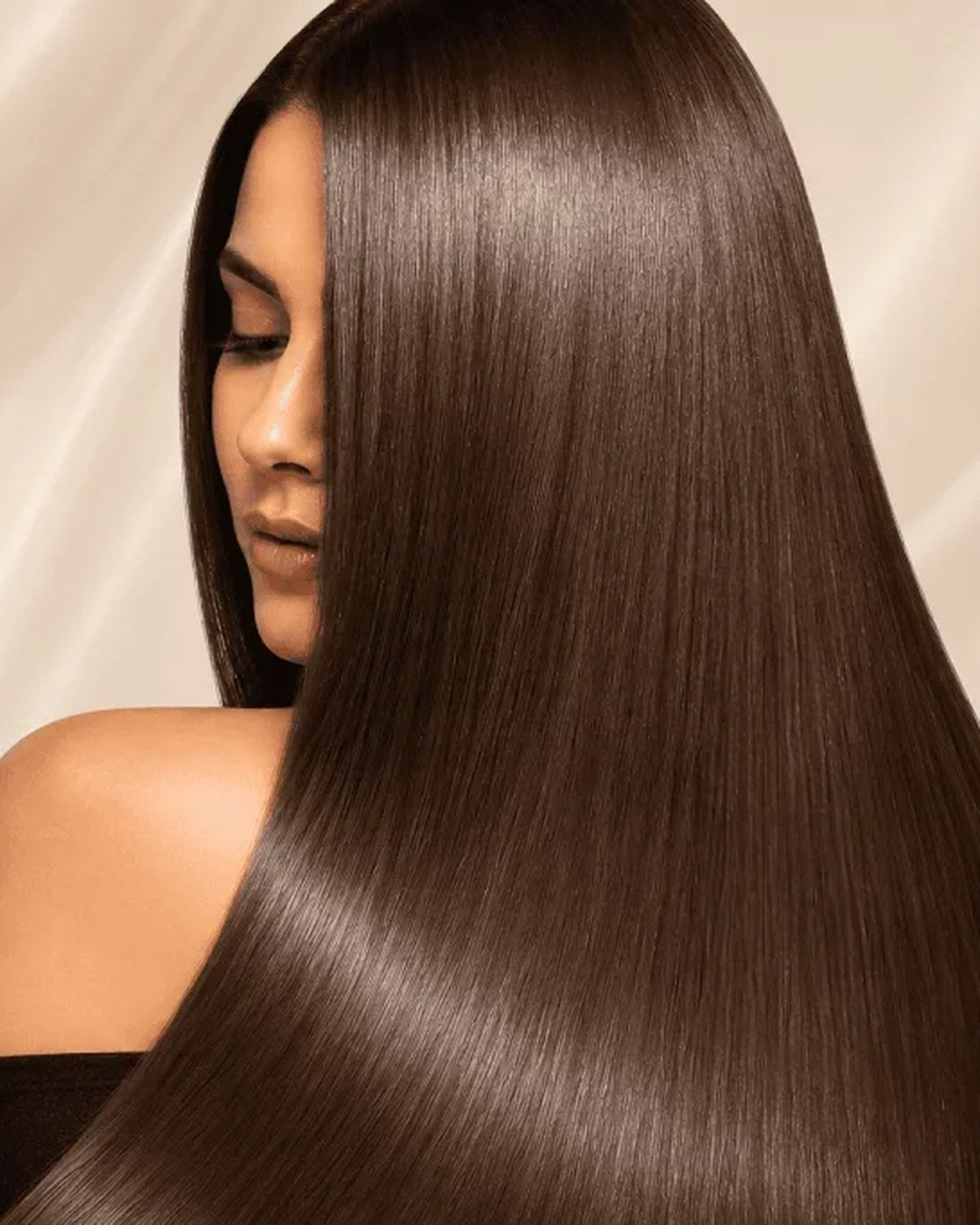 Woman with long, sleek, glossy brown hair after a keratin smoothing treatment, against a soft cream satin background