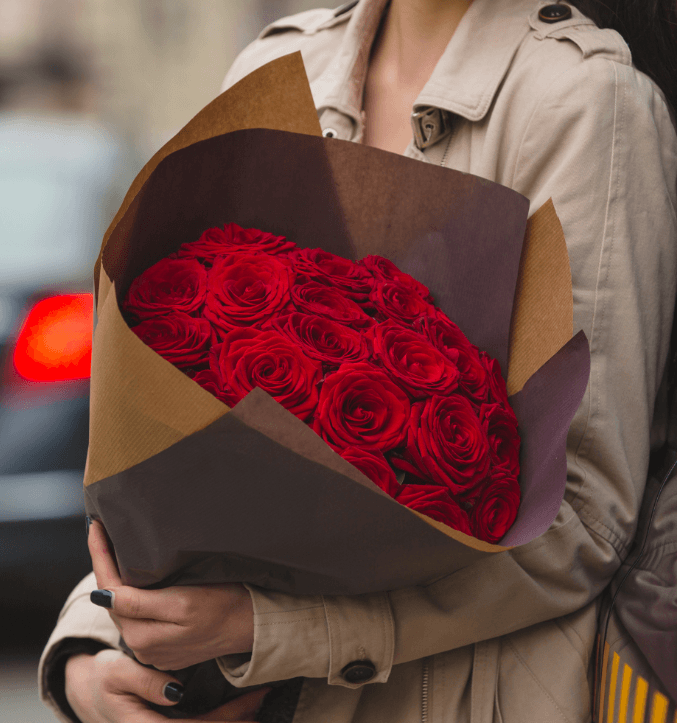 Person holding a bouquet of red roses wrapped in brown paper.